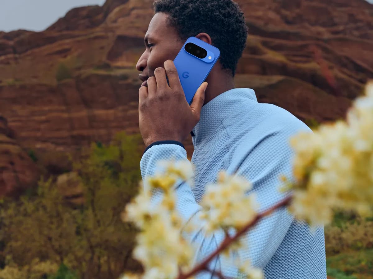 A person holding a Google Pixel 10 in Indigo to their ear outdoors.