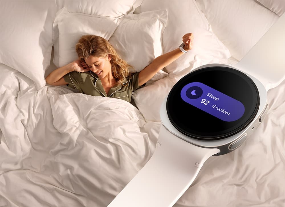 Samsung Galaxy Watch8 in silver with a white band, worn in bed, displaying a sleep score of 92.